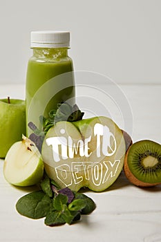 bottle of green detox smoothie with apples, kiwi and mint and on white wooden surface, time to detox inscription