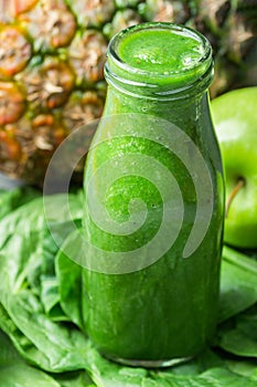 Bottle with Green Fresh Raw Smoothie from Leafy Greens Vegetables Fruits Apples Pineapple Bananas Kiwi Zucchini on Spinach leaves