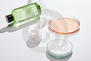 Bottle with green liquid, jar with white cosmetic cream, laboratory glassware with liquid and rose petal on white