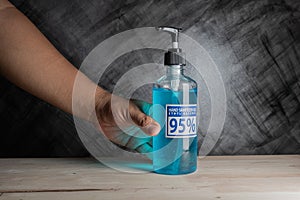 bottle of hand sanitizer blue gel with ingredient ethyl alcohol 95% in hand human on wooden table with dark background