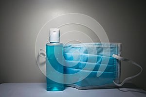 Bottle of hand sanitizer gel and a surgical mask required for Coronavirus infection prevention placed on a white table and a white