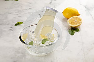 A bottle of healthy Lemon and Mint Juice served in iced cube bowl side view on grey background