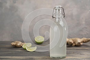 Bottle with homemade ginger ale, lemon and gingerroot on gray background.