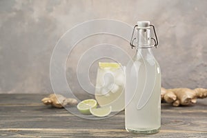 Bottle with homemade ginger ale, lemon and gingerroot on gray background.