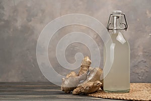 Bottle with homemade ginger ale, lemon and gingerroot on gray background. photo