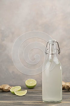 Bottle with homemade ginger ale, lemon and gingerroot on gray background. photo