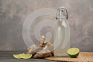 Bottle with homemade ginger ale, lemon and gingerroot on gray background. photo