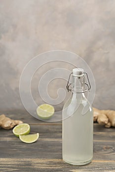 Bottle with homemade ginger ale, lemon and gingerroot on gray background. photo