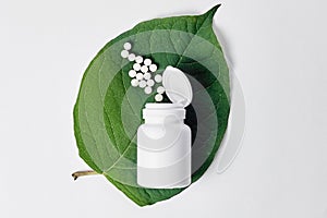 Bottle with homeopathic pills on green plant leaf. Homeopathy, naturopathy and alternative herbal medicine