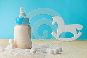Bottle with infant formula milk near rocker horse toy and sugar