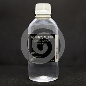 Bottle of ISOPROPYL ALCOHOL for medical and industrial use 99% pure on a black background. colorless, flammable compound