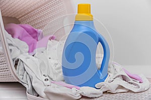 Bottle of laundry detergent in the basket with dirty baby clothes.