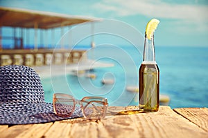 Bottle of light beer with slice of lemon standing on wooden table on beach bar with sea background.