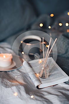 Bottle with liquid home fragrance and wooden bamboo sticks, scentes burn candle and cup of black tea over glow lights at backgroun