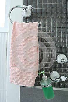 Bottle of liquid soap and pink towels have hanging on a clothesline of bathroom interior.