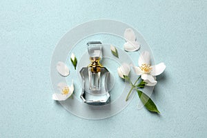 Bottle of luxury perfume and fresh jasmine flowers on light blue background, flat lay