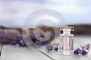 Bottle of luxury perfume and lavender flowers on white wooden table outdoors