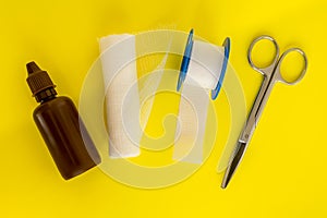 Bottle with medicine iodine, roll of bandage, adhesive plaster and medical scissors on a yellow background