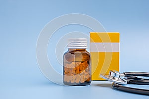 Bottle of medicine tablets, paper box, and a stethoscope isolated on a light blue background.