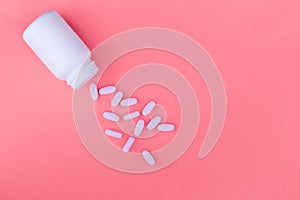 Bottle of medicines and scattered pills on a pastel pink background. Ripped vitamins on a bright background