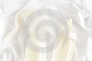 Bottle of milk and manual breast pump for newborn baby over white silk satin background. Top view. Maternity and baby care concept