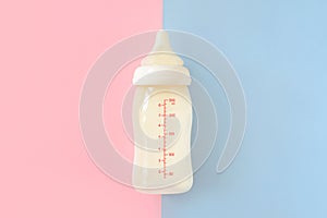 Bottle of milk for newborn baby over pink and blue pastel colors background. Maternity and baby care concept. Top view.