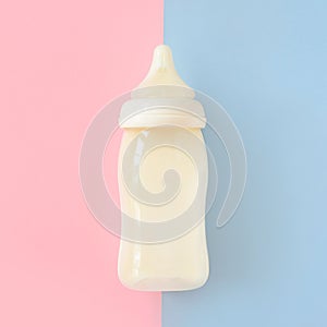 Bottle of milk for newborn baby over pink and blue pastel colors background. Maternity and baby care concept. Top view.