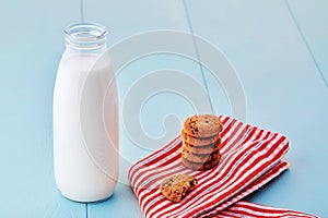 Bottle of milk and pile of chocolate chip cookies on napkin on blue wooden table