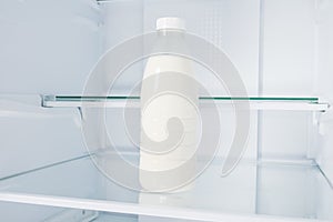 A bottle of milk on a shelf in an empty refrigerator