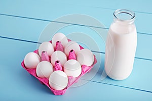 Bottle of milk and white eggs in a pink filler tray on turquoise wooden country kitchen table