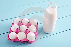 Bottle of milk and white eggs in a pink filler tray on turquoise wooden country kitchen table.