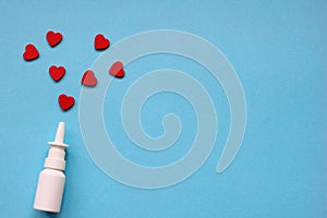 A bottle of nasal spray on a blue background and red hearts around it. Treatment with love. Health care. Vasoconstrictors