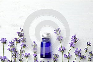 Bottle with natural essential oil and lavender flowers on white wooden background. Space for text