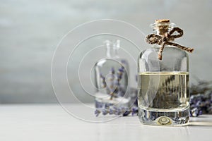 Bottle of natural essential oil and lavender flowers on white wooden table