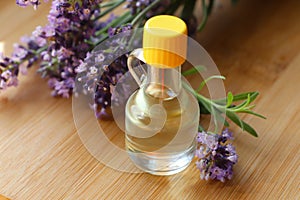 Bottle of natural essential oil and lavender flowers on wooden table, closeup