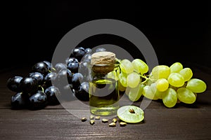 Bottle of natural grape seed oil, bunch of blue and white grapes on a dark wooden table. Organic cosmetic