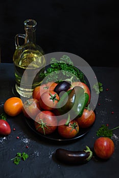 Bottle of olive oil and farm vegetables, tomatoes peppers and eggplant in black key