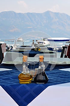 bottle of olive oil and italian balsamic vinegar on blue tablecloth in the open air restaurant on embankment with bay and yacht o