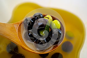 Bottle of olive oil and a wooden spoon with olives on a table