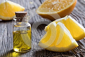 A bottle of orange essential oil with oranges on a wooden table