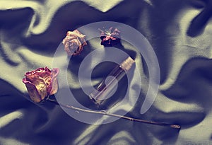 Bottle of perfume and buds of dried roses on a gray silk backg