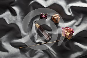 A bottle of perfume and buds of dried roses on a gray silk background. Romantic look. Top view