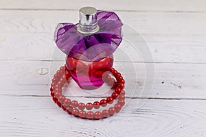 Bottle of perfume and red beads necklace on white wooden background