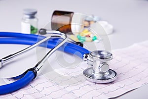 Bottle of pills and Medical stethoscope lying on cardiogram chart closeup. Medical help, prophylaxis, disease prevention