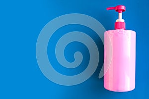 Bottle with pink dishwashing liquid on blue background. Minimal concept.