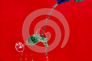 Bottle pouring green liquid into an overflowing glass cup