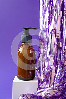 Bottle with pump for beauty product mockup and holiday tinsel on cube podium on violet background, vertical