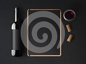 Bottle of red wine with a black label on a dark background, a wine menu template and a glass of wine.