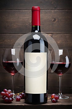 Bottle of red wine with blank label and grapes on wooden background