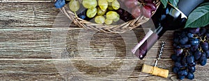 Bottle with red wine, corkscrew, blue grapes in basket, leaves on a wooden table. Wine background with copy space. Top view, flat